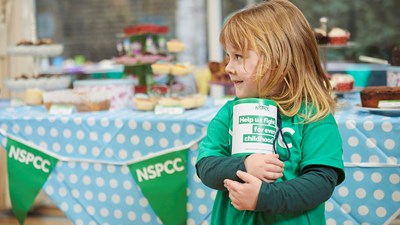 A child smiling while holding an NSPCC collection box.