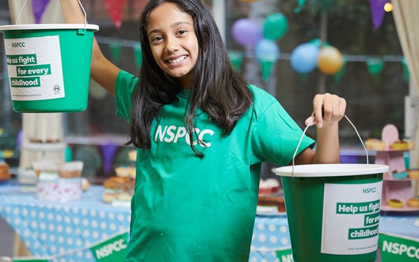 A teenage girl smiling while holding an NSPCC fundraising bucket.