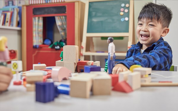 A young boy smiling while playing with toys at nursery.