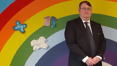 NSPCC volunteer Hywell Peterson  standing in front of wall with a rainbow on it