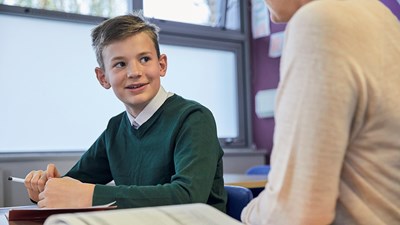 A secondary school pupil smiling while having a conversation with their teacher.