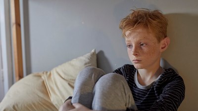 Boy sitting on his bed looking sad