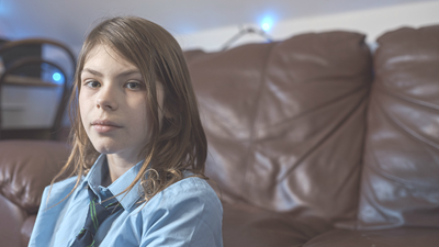Young girl sitting indoors, looking directly at camera