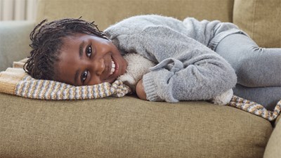 A young girl smiling while lying down on a sofa.