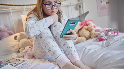 Young girl checking phone in bed surrounded by teddy bears