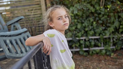A young girl leaning back against railings while staring into the camera.