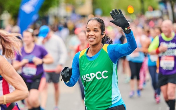Woman in NSPCC vest running and smiling in Brighton Marathon