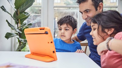 A parent/carer smiling while using a computer tablet with their children.