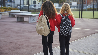 Two girls in school uniform walking home together through a playground