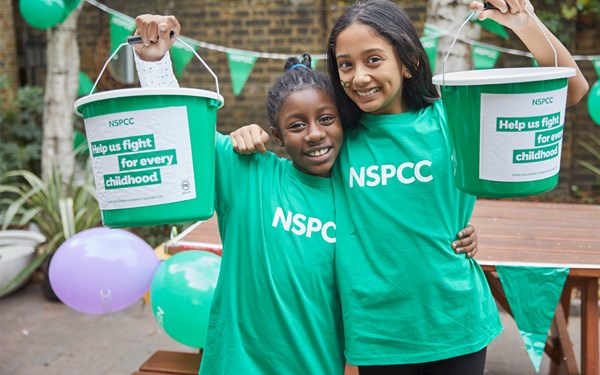 Two young girls holding fundraising buckets for the NSPCC